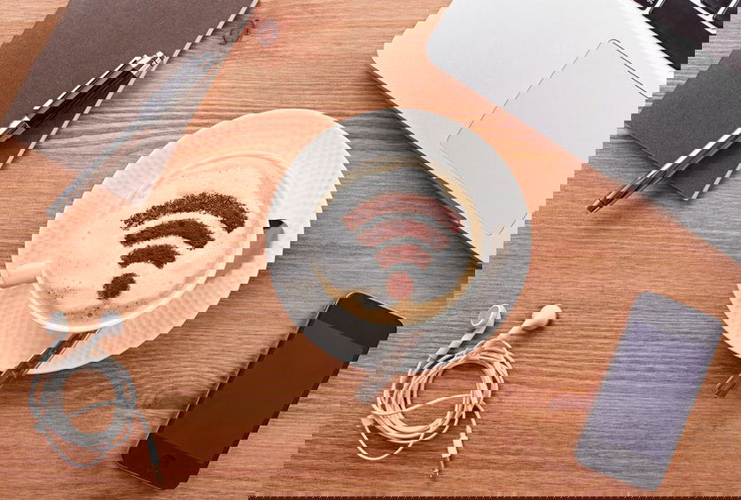 Mesa de madeira com computador, celular, fone e café com espuma e desenho do ícone de wi-fi